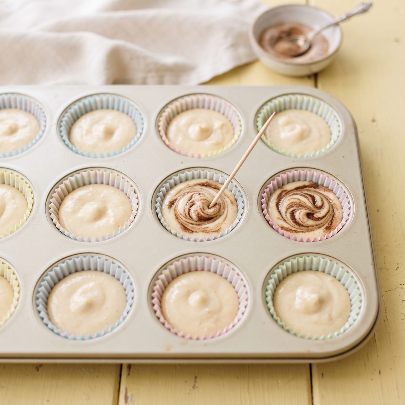 Cinnamon sugar being swirled into apple cider cupcake batter in a muffin tin