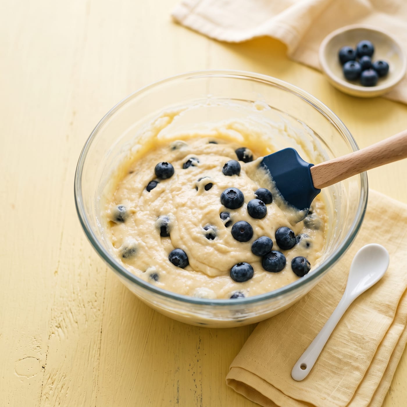 Blueberry muffin batter with fresh blueberries being folded in with a spatula