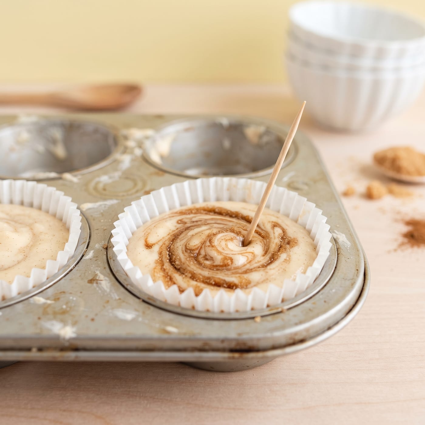 Cinnamon filling being swirled through brown sugar cupcake batter with a toothpick before baking