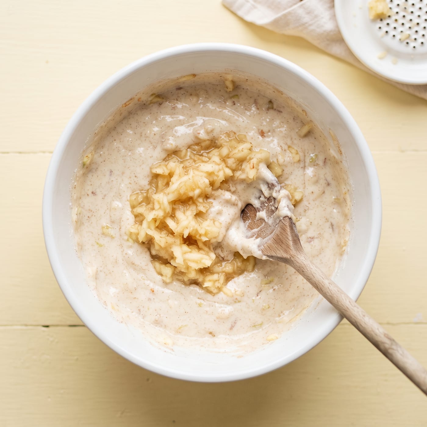 Grated apple being folded into cupcake batter in a mixing bowl
