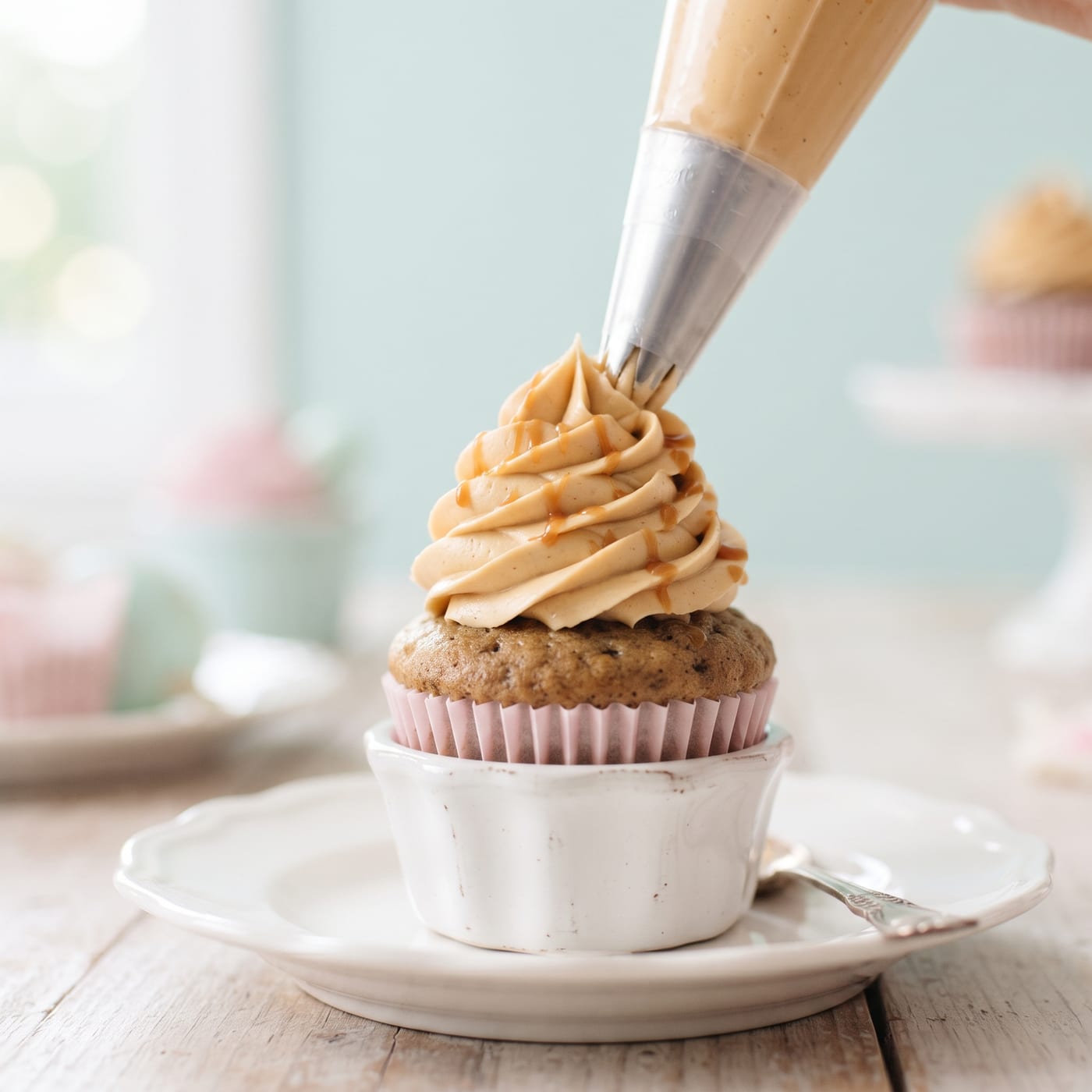 Piping caramel buttercream in a tall swirl onto an espresso vanilla cupcake