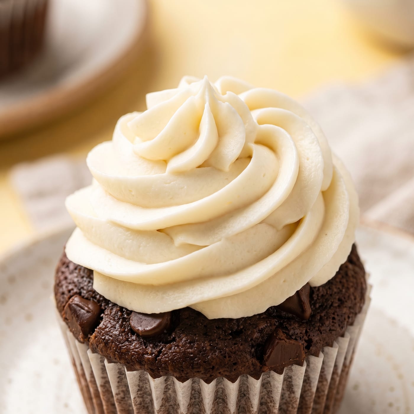 Close up of milk frosting swirl showing soft texture with a chocolate chip cupcake crumb visible