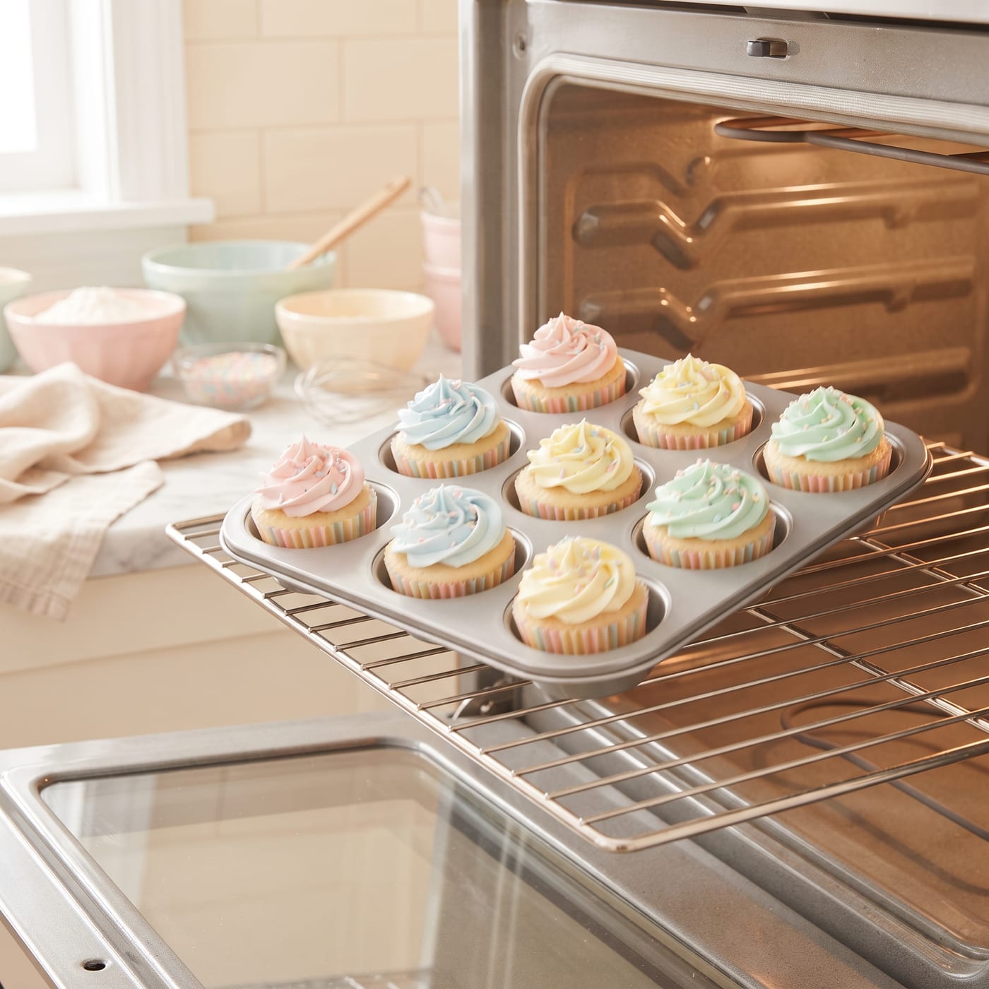 Baker's hands rotating a cupcake tray between oven racks midway through baking