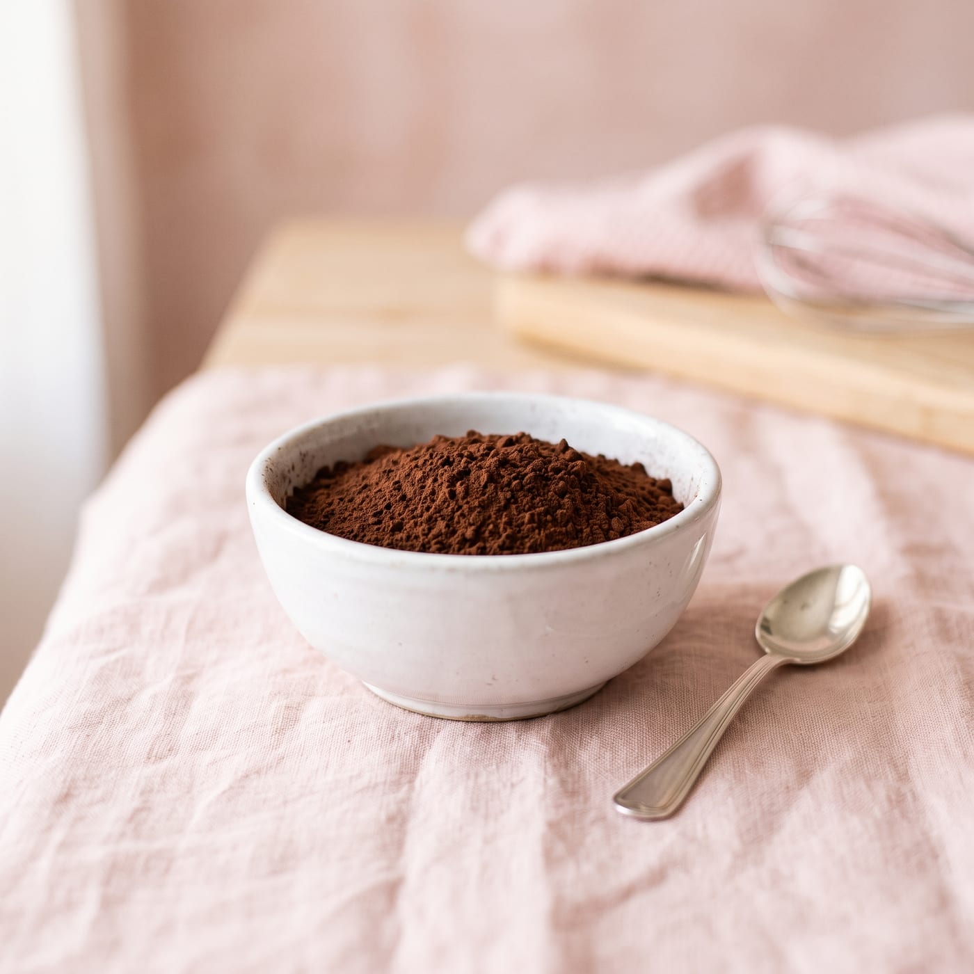 Close up of cocoa powder texture in a small white bowl with a spoon resting beside it