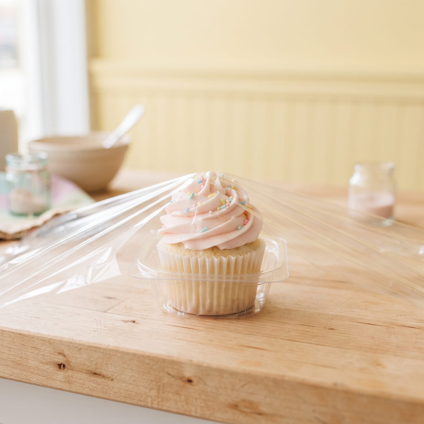 Cupcake being wrapped in plastic wrap before freezing on a light wood counter