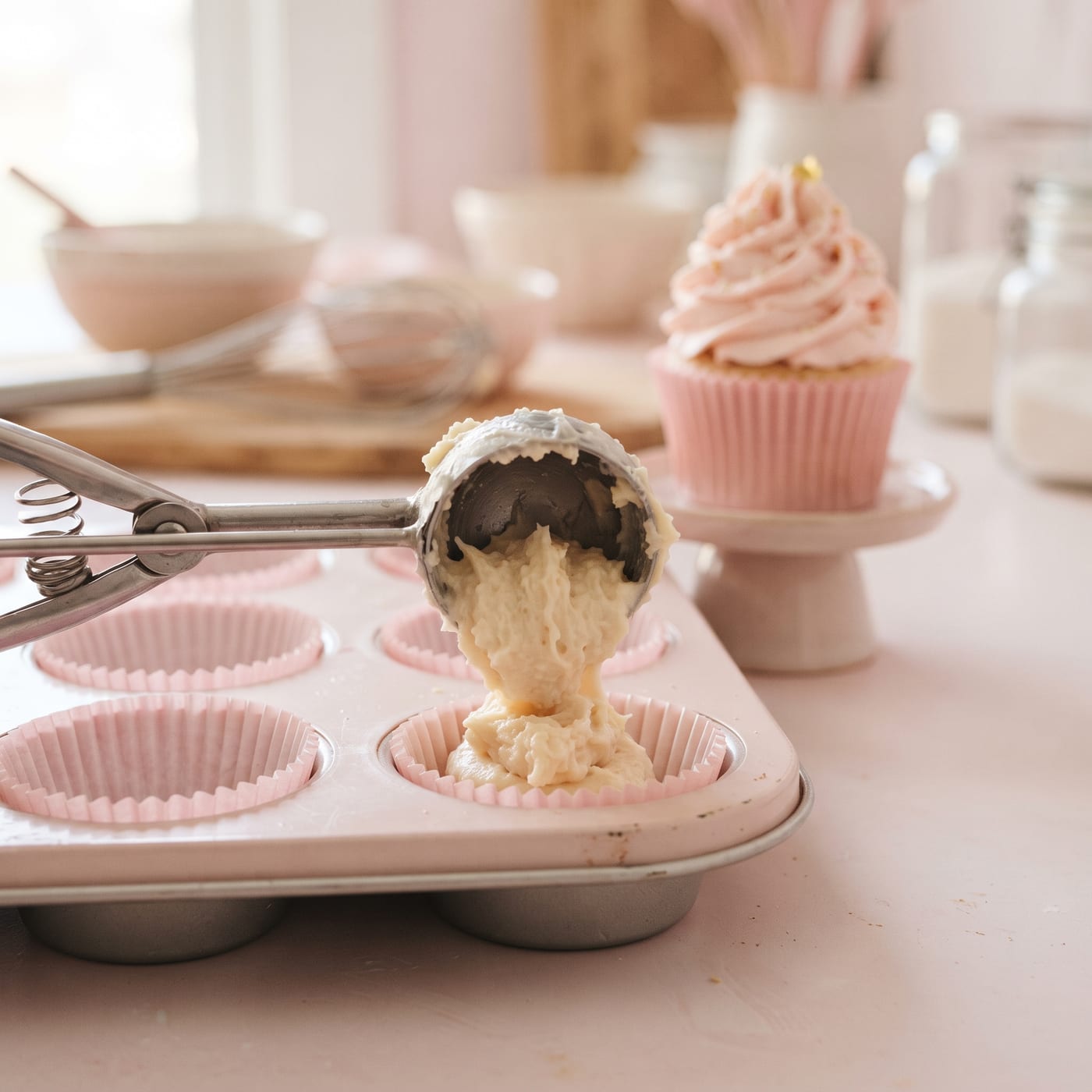 Cookie scoop portioning cupcake batter into paper liners for even fill levels
