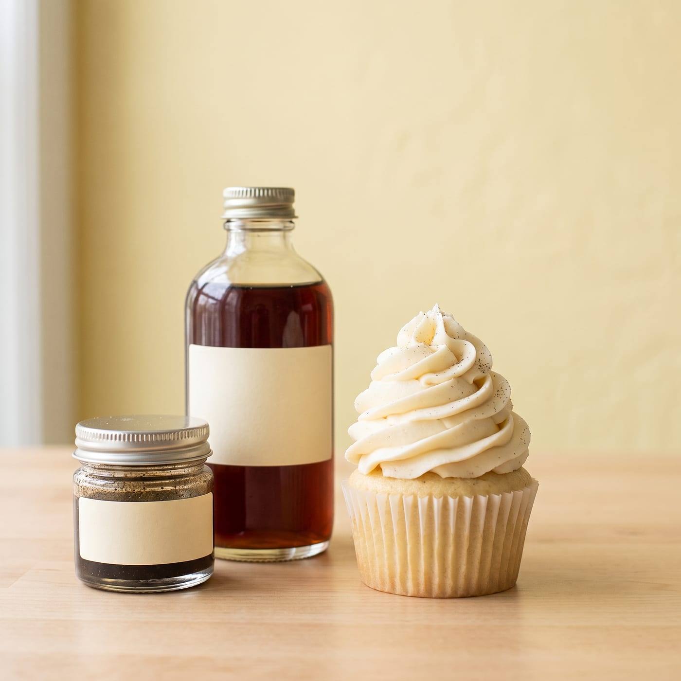 Bottles of pure vanilla extract and vanilla bean paste next to a frosted cupcake