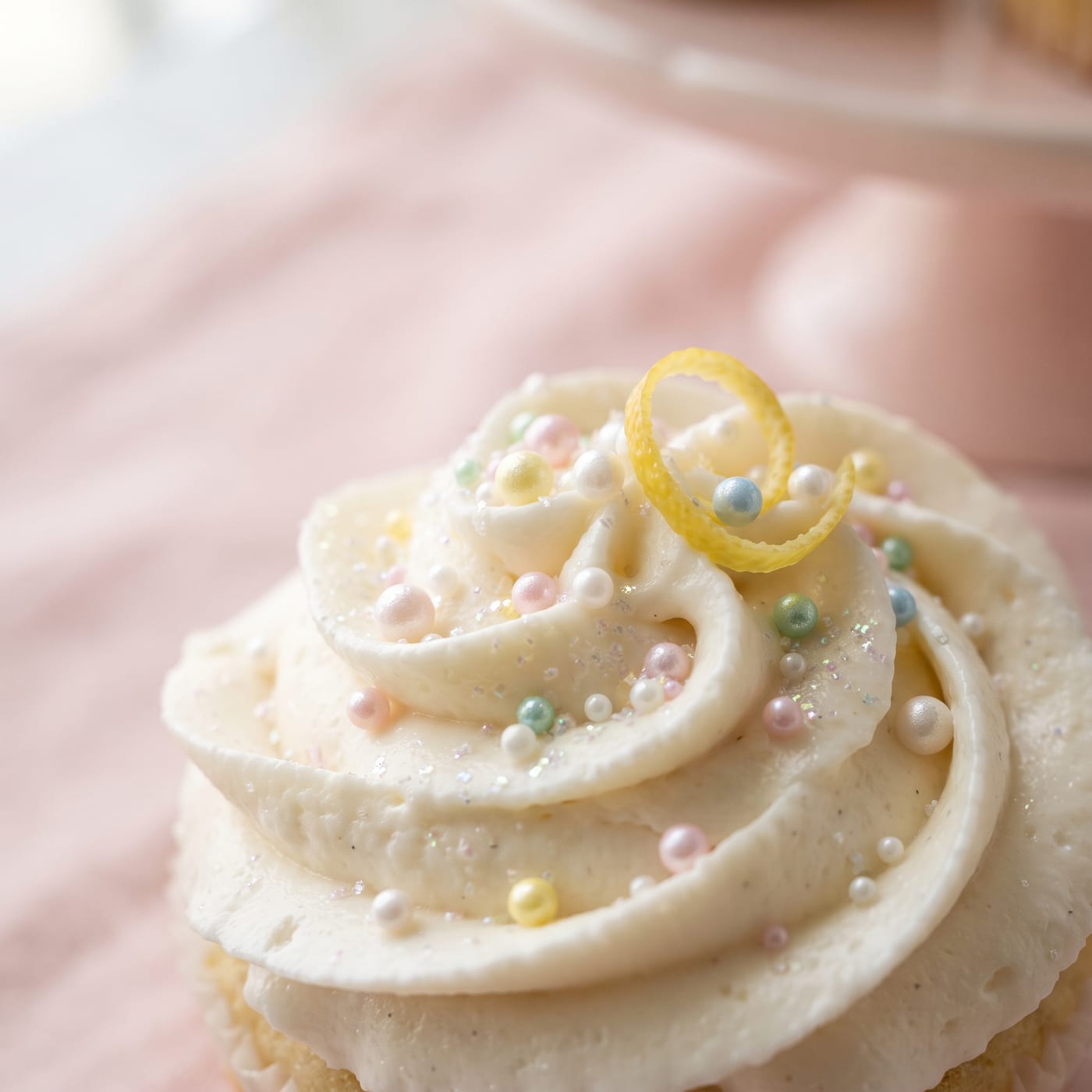 Close up of sugar pearls and citrus zest curl placed on frosting swirl
