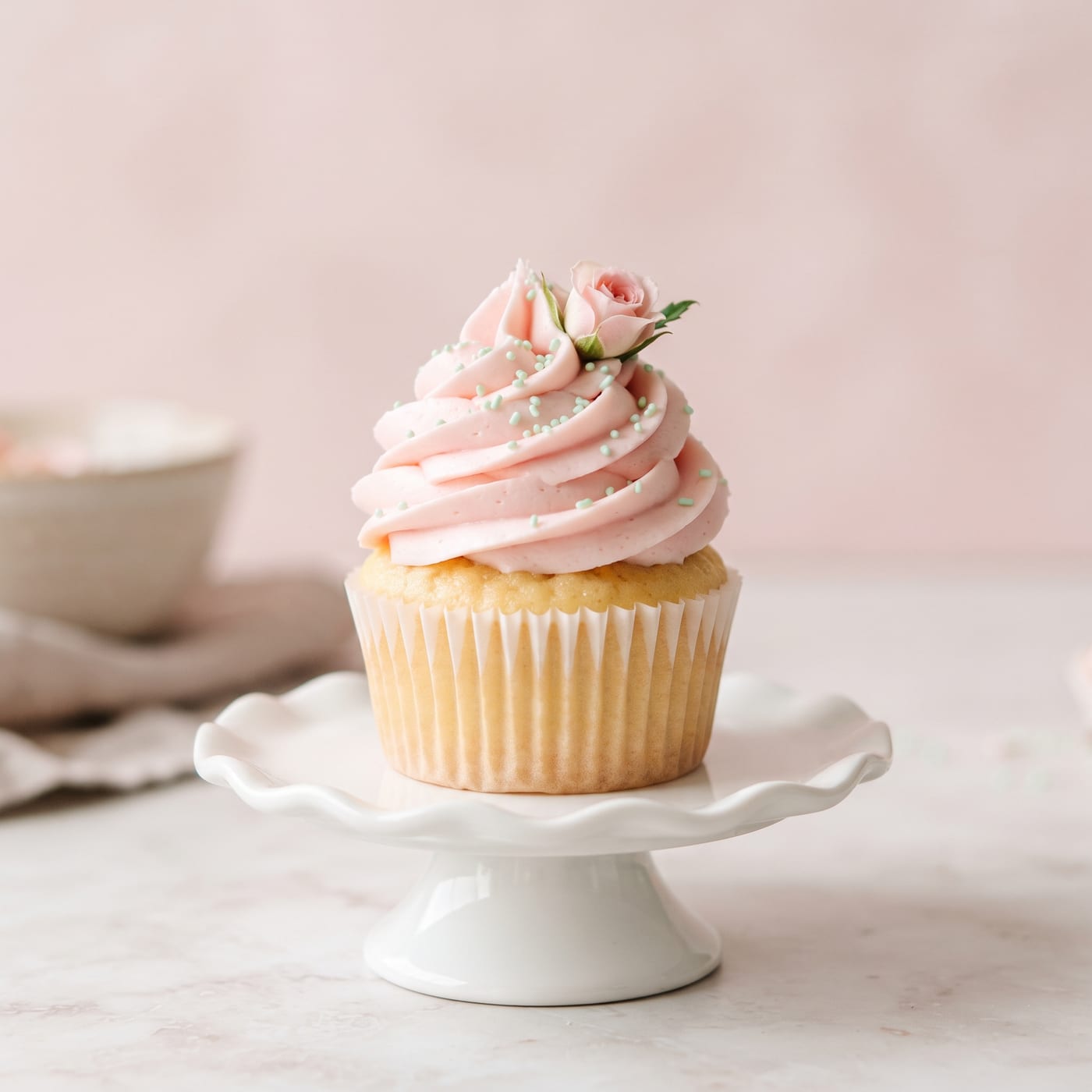 Close up of a pastel pink spring cupcake topped with a small edible flower and green sprinkles