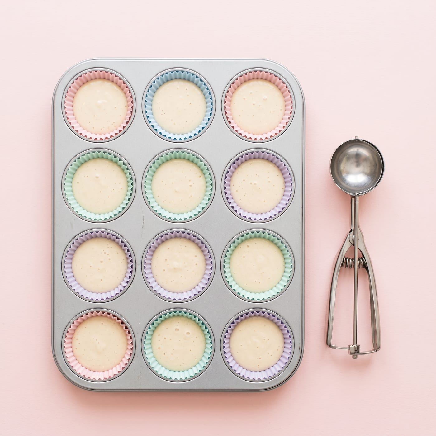 Cupcake liners in a tin filled evenly with pale batter using an ice cream scoop