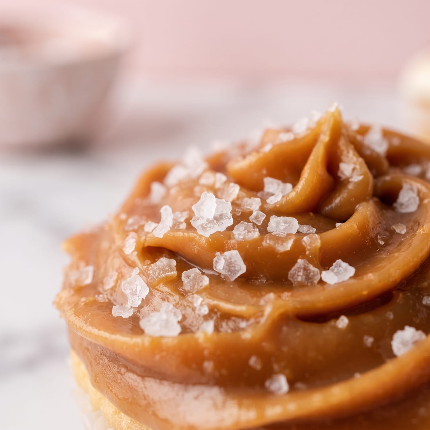 Close up of flaky salt crystals resting on swirled caramel frosting