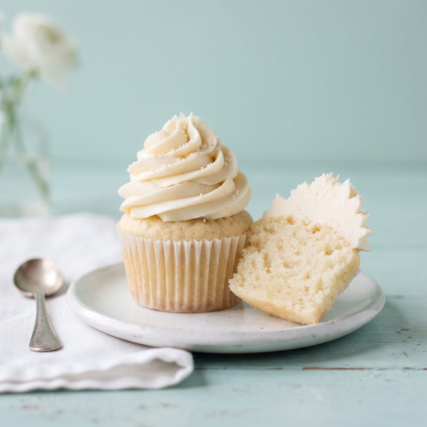 Tall swirled vanilla cupcake on a pale aqua background showing a light airy crumb