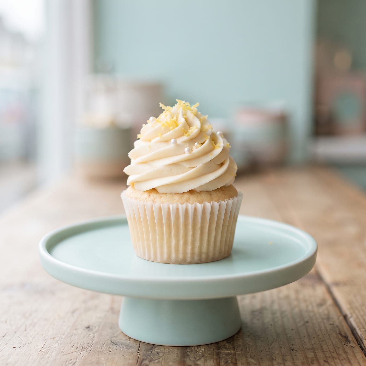 Vanilla cupcake with tall swirled frosting and lemon zest garnish on pale aqua background