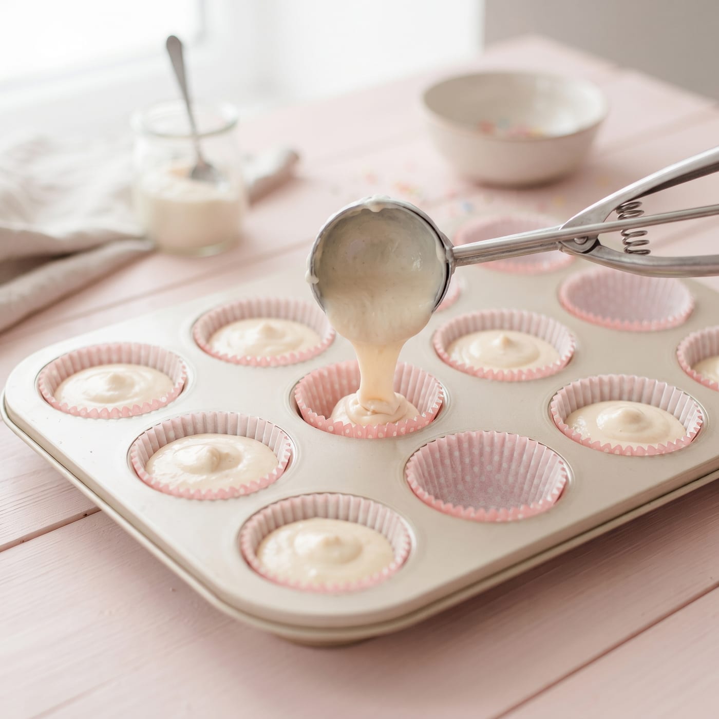 Ice cream scoop portioning cupcake batter into a lined muffin pan