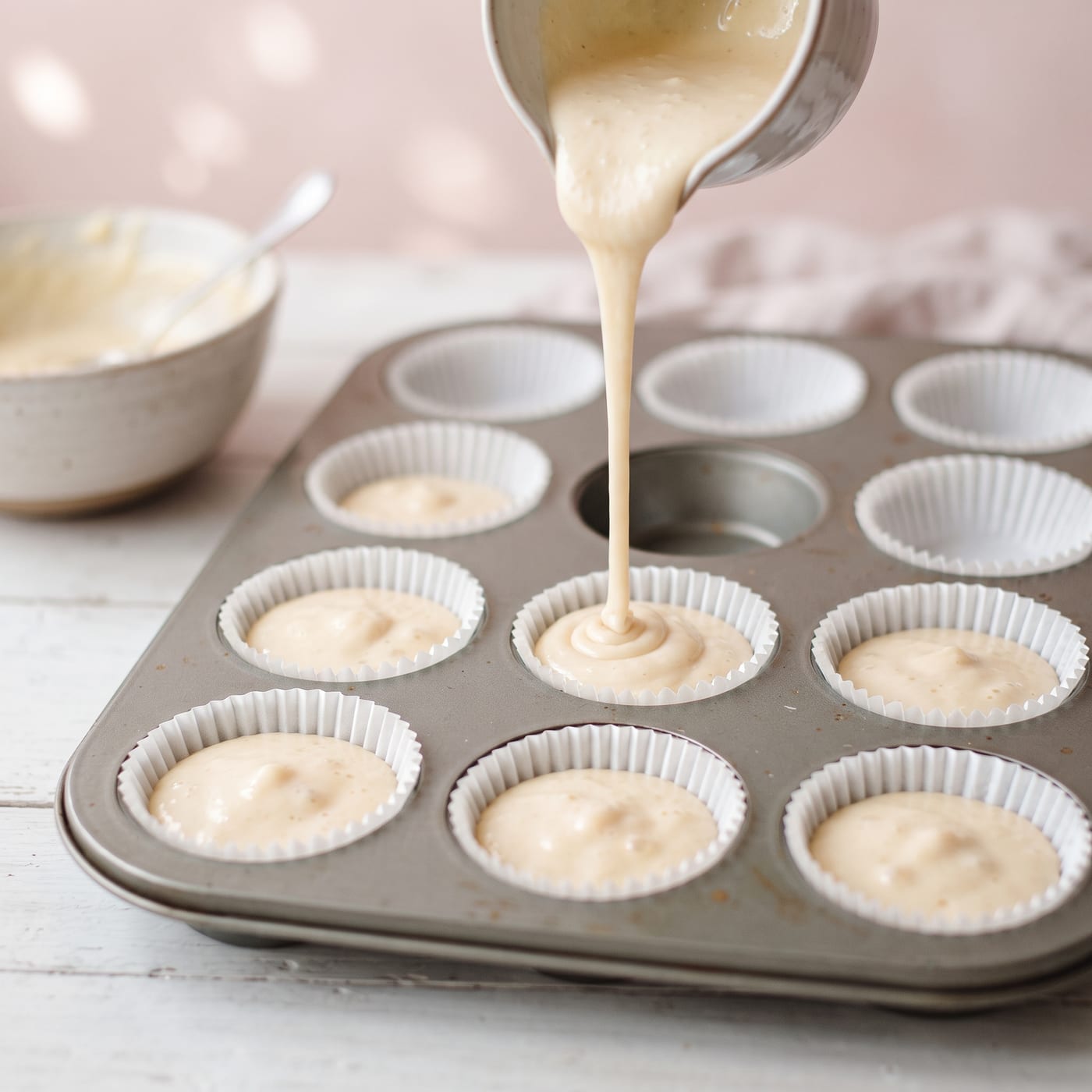 Smooth pale cupcake batter being poured into paper liners showing even glossy texture