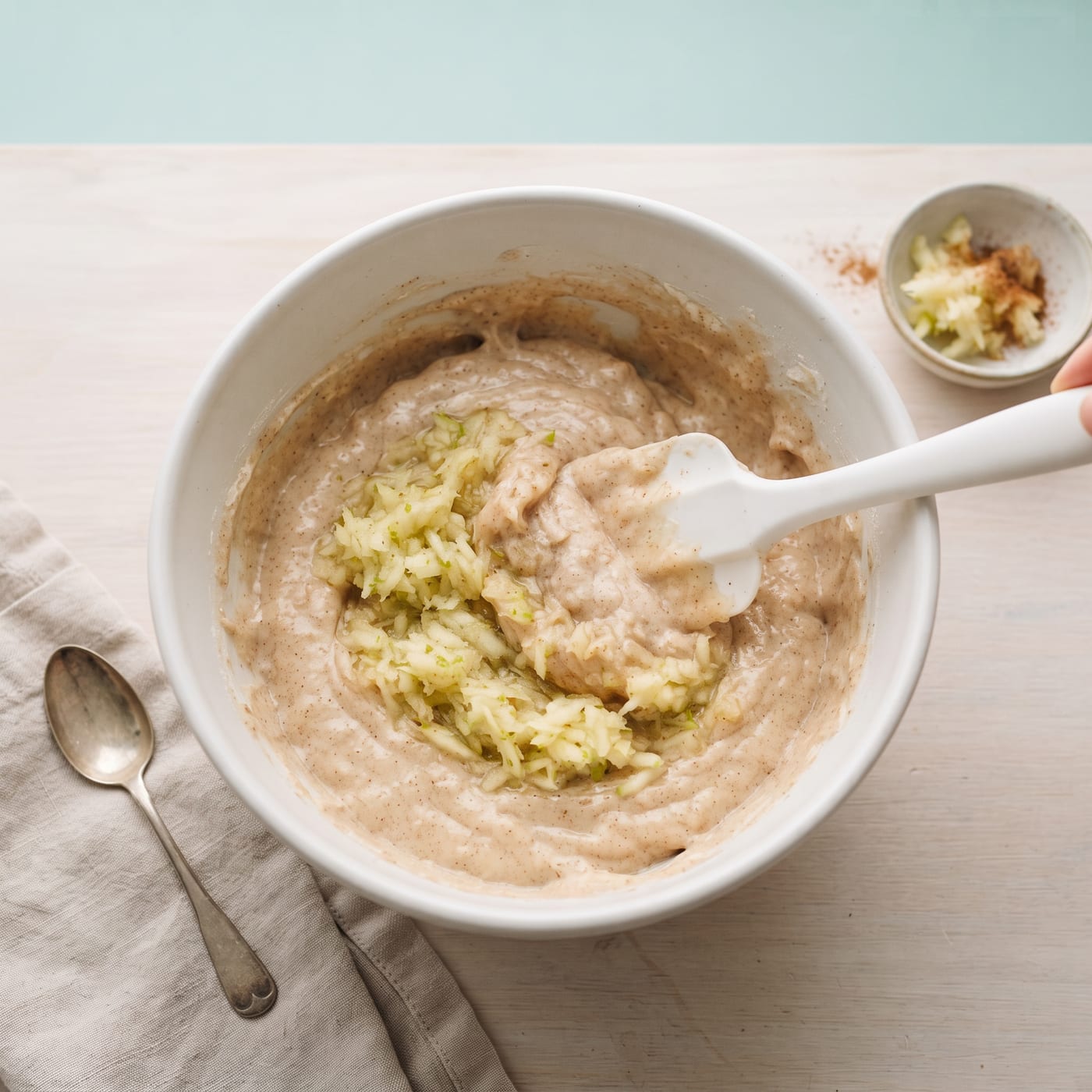Grated apple being folded into cupcake batter in a mixing bowl