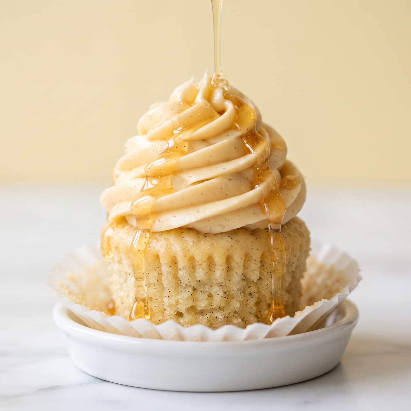 Close up of honey drizzling over a frosted vanilla bean cupcake