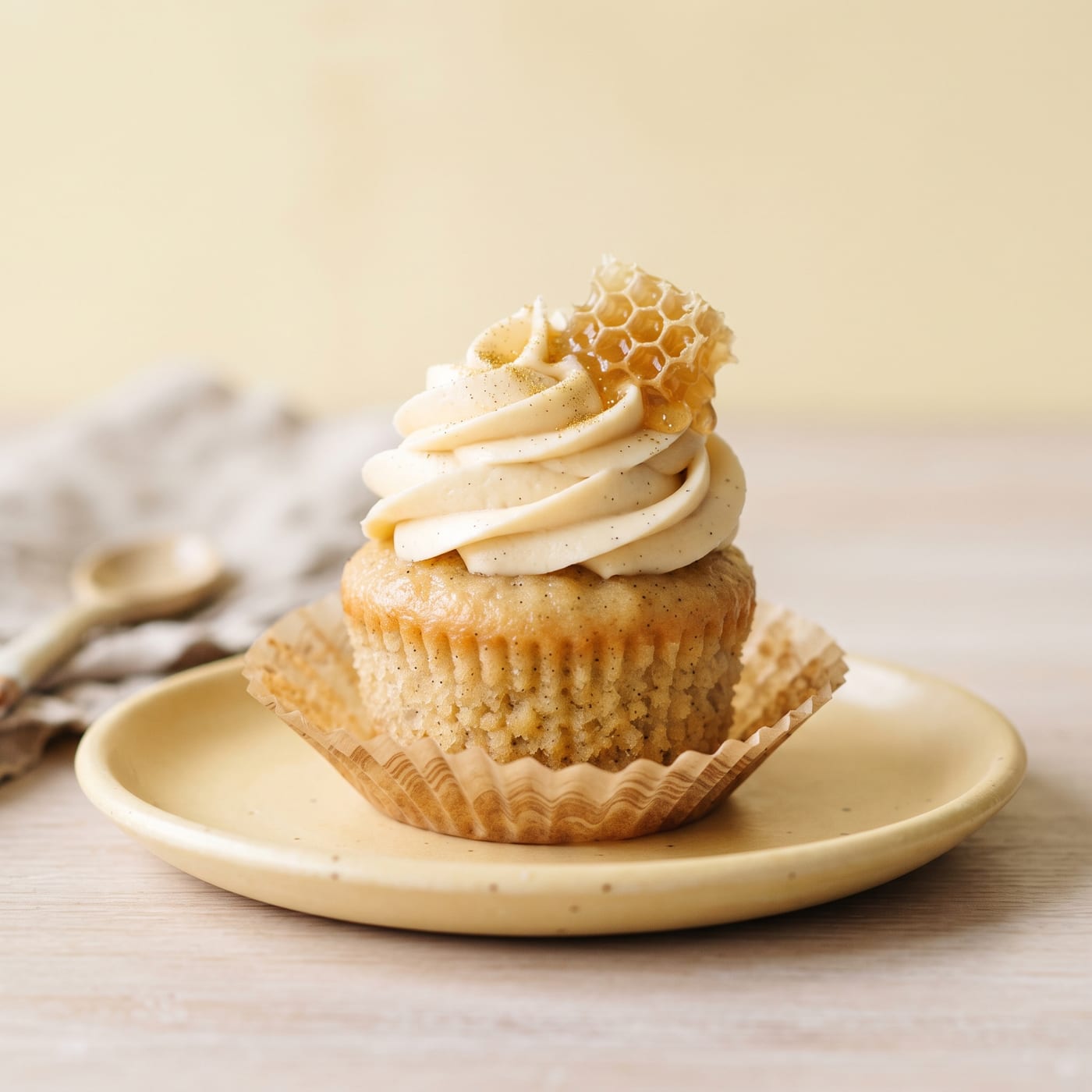 Honey vanilla bean cupcake with tall swirled honey frosting on a pastel background