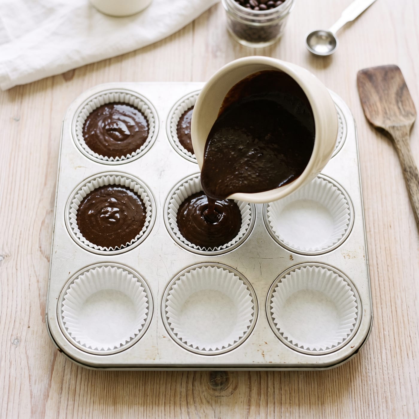 Espresso cupcake batter being poured into paper liners in a muffin pan