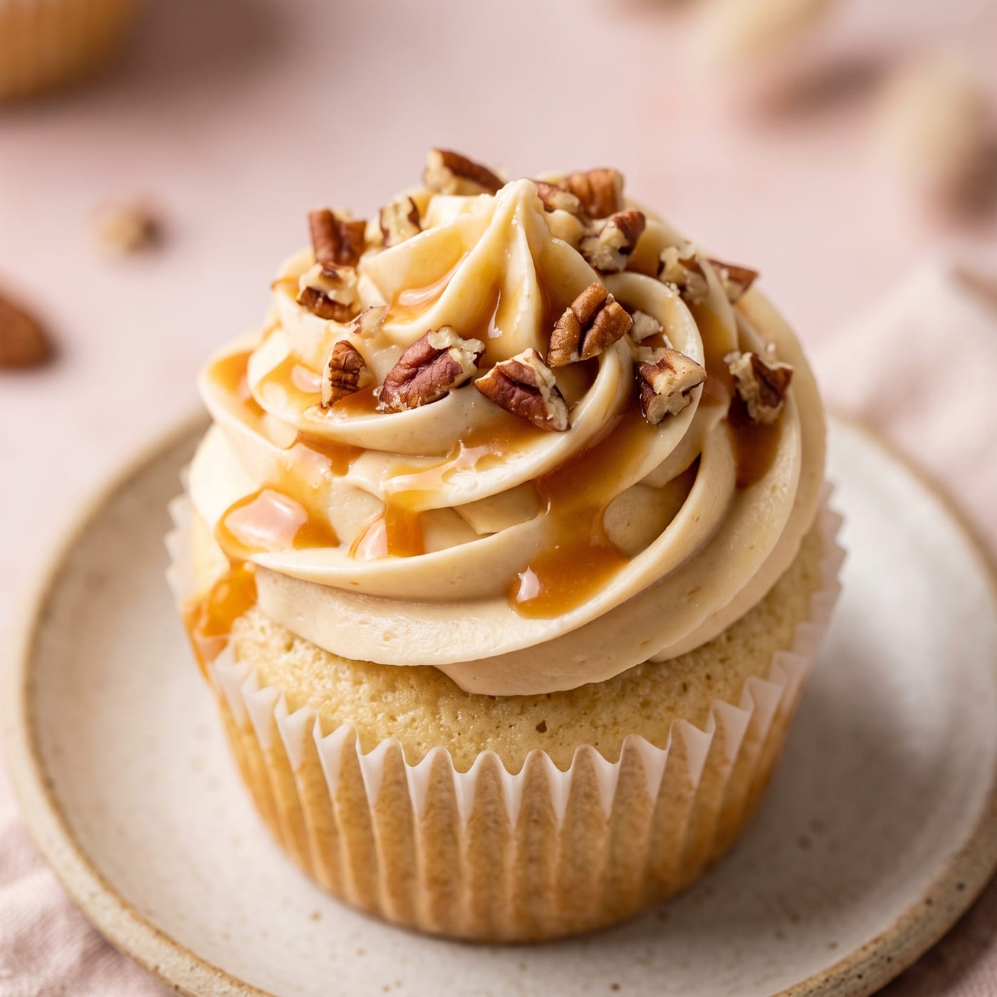 Close up of chopped pecans and caramel drizzle on top of a frosted keto cupcake