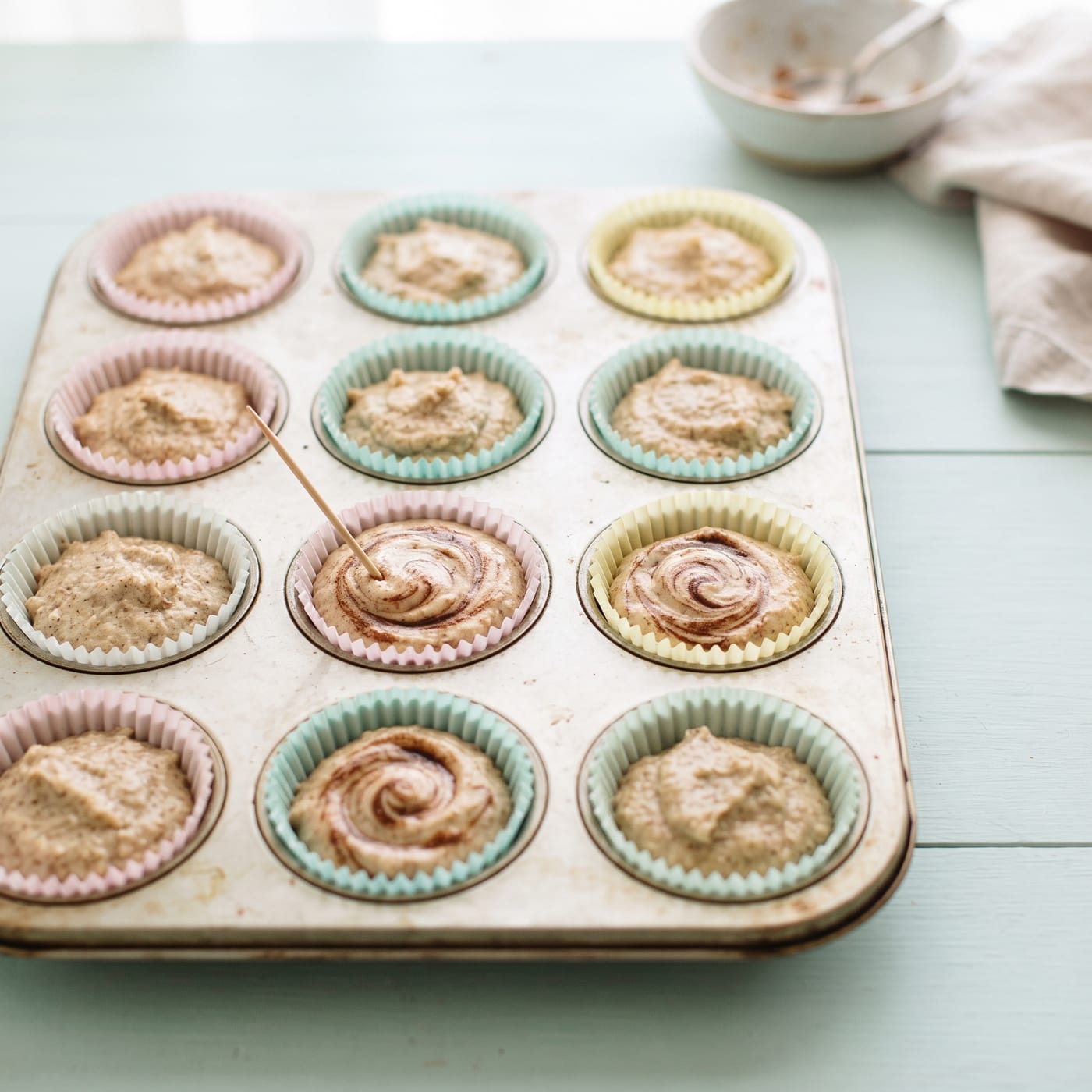 Cinnamon swirl being drizzled and swirled into keto cupcake batter with a toothpick before baking