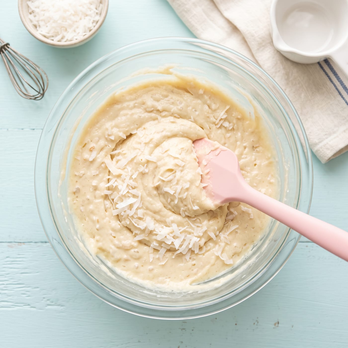 Coconut cupcake batter with shredded coconut being folded in a glass bowl