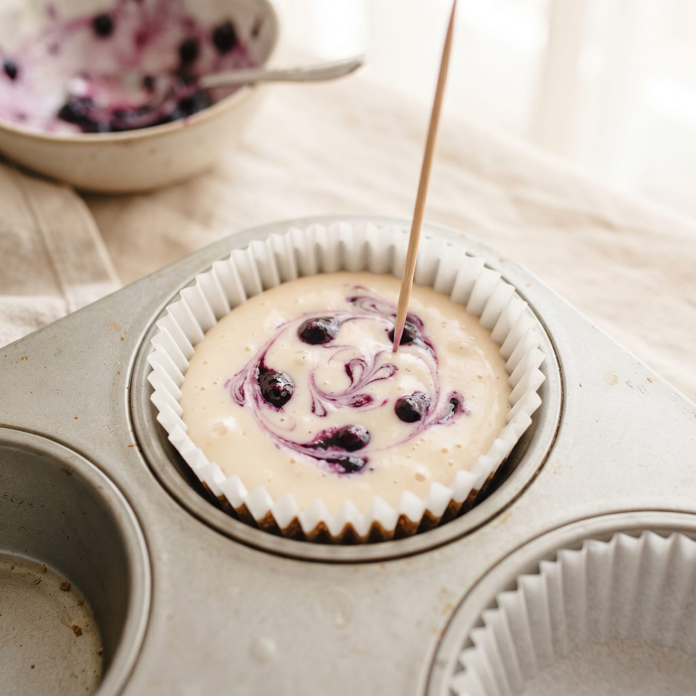 Blueberry mixture being swirled into cheesecake batter in a cupcake liner before baking