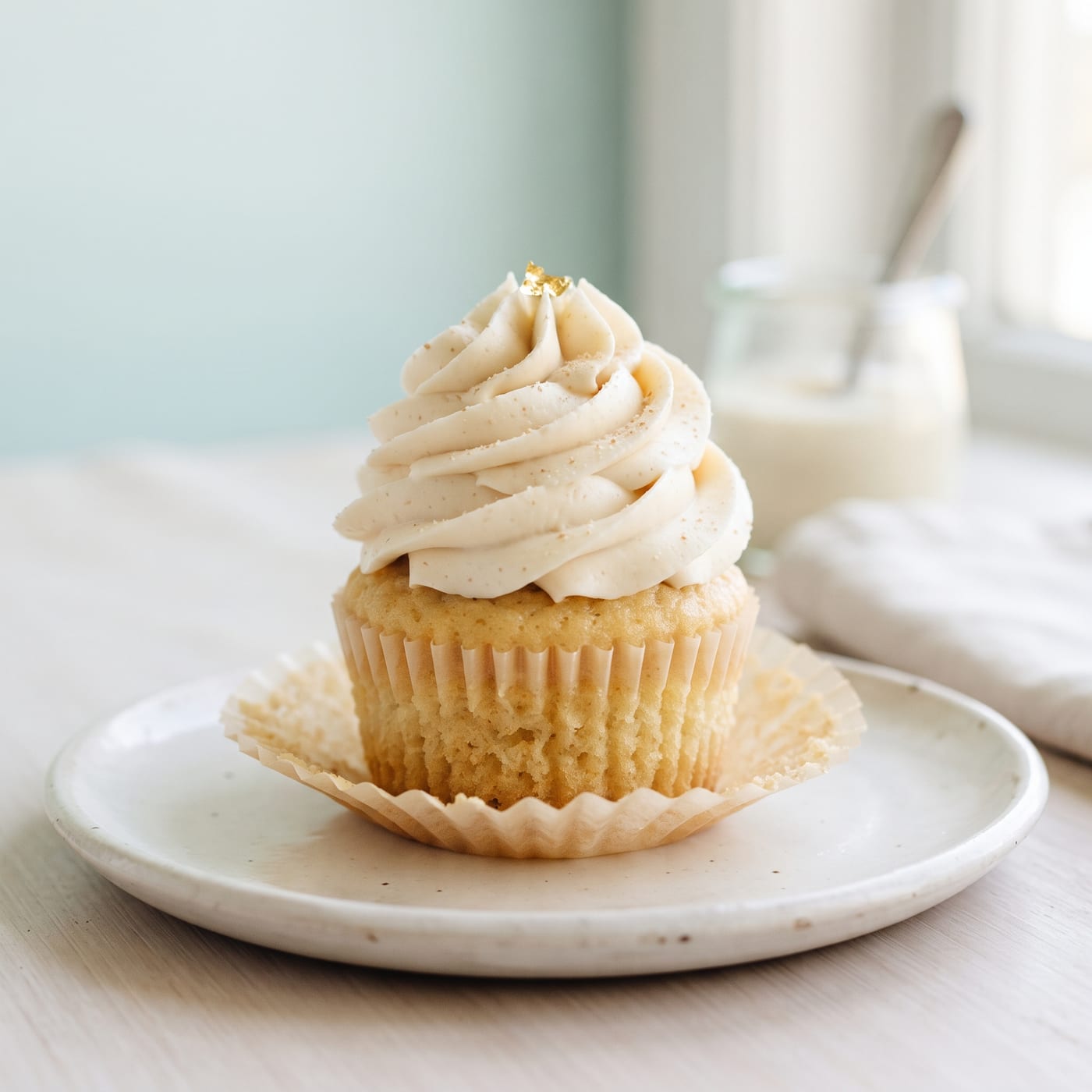 Keto maple butter cupcake with tall swirled vanilla frosting on a pale aqua background