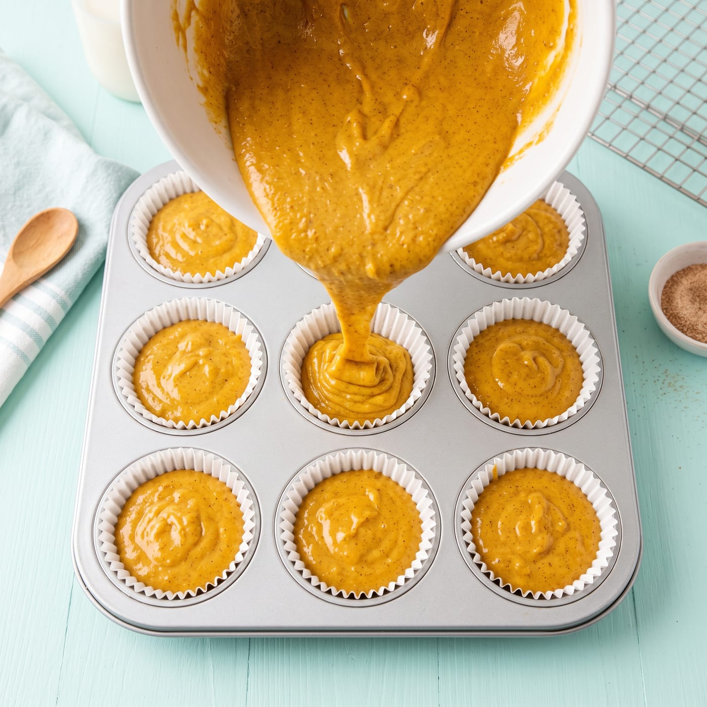 Pumpkin spice cupcake batter being poured into paper lined muffin pan before baking