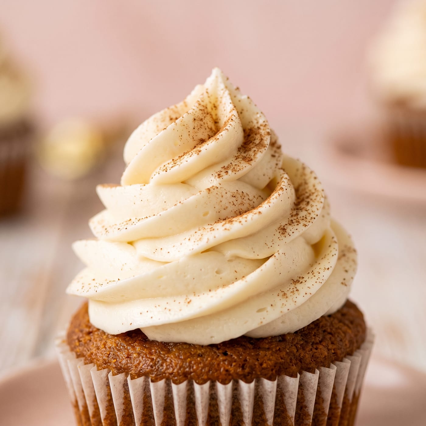 Close up of cream cheese frosting swirl on keto pumpkin spice cupcake showing texture and cinnamon garnish