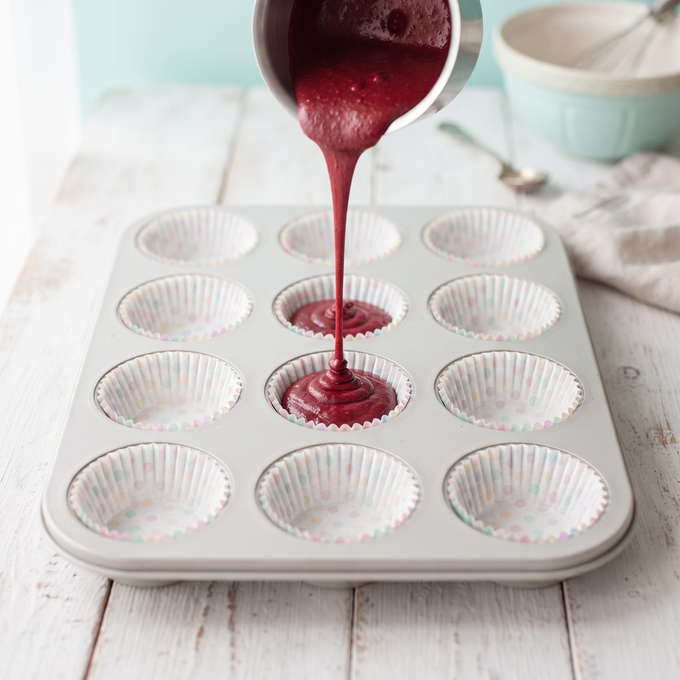 Red velvet keto batter being poured into a lined muffin pan
