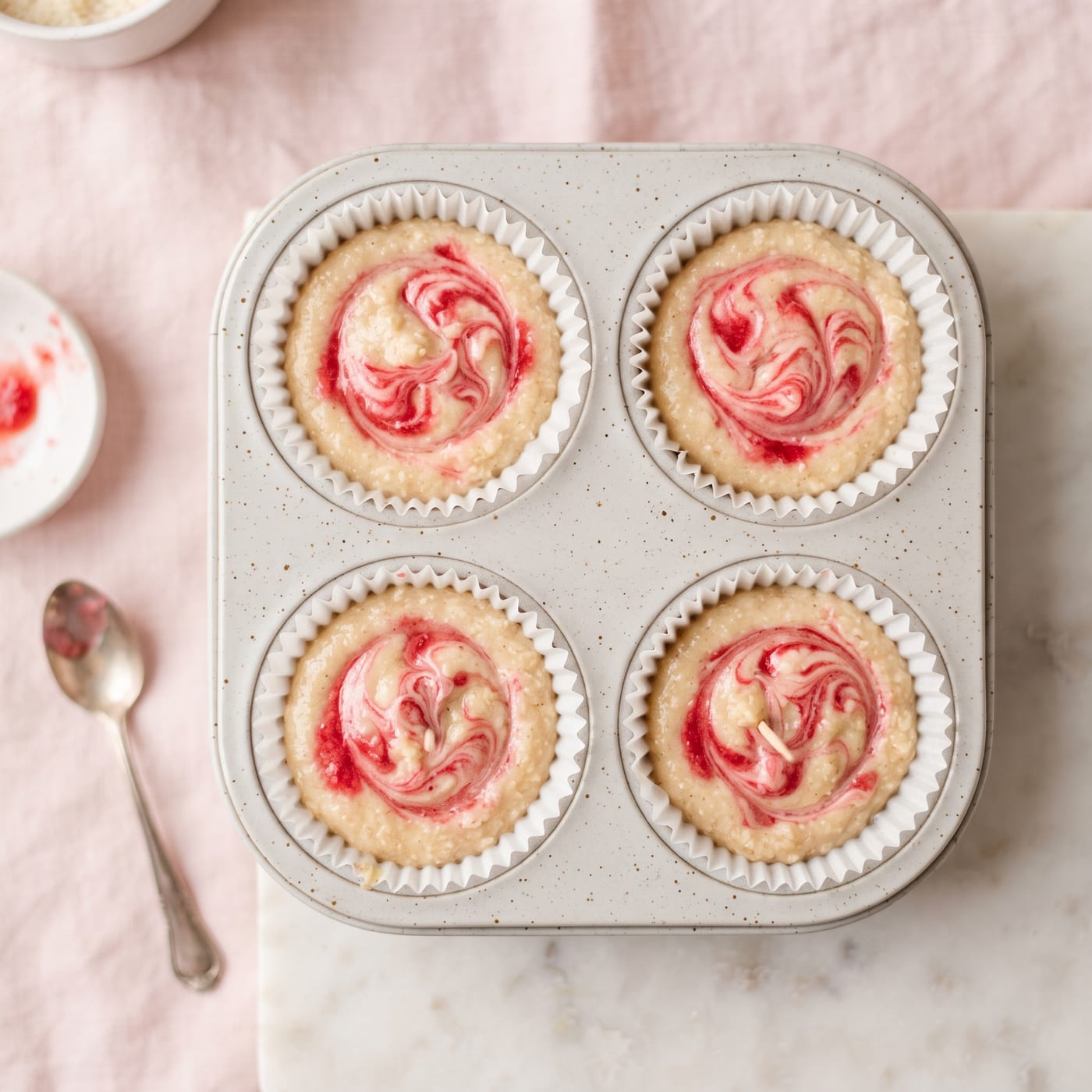 Strawberry puree being swirled into pale keto cupcake batter with a toothpick before baking