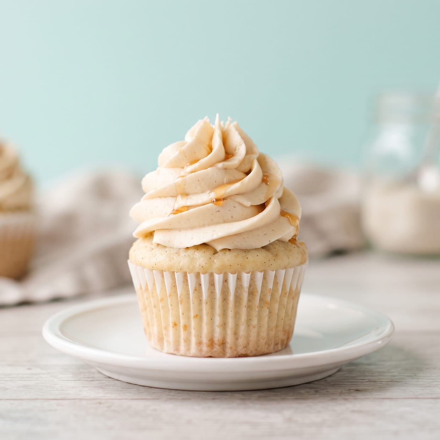 Maple vanilla cupcake with tall swirled maple frosting on a pale aqua background