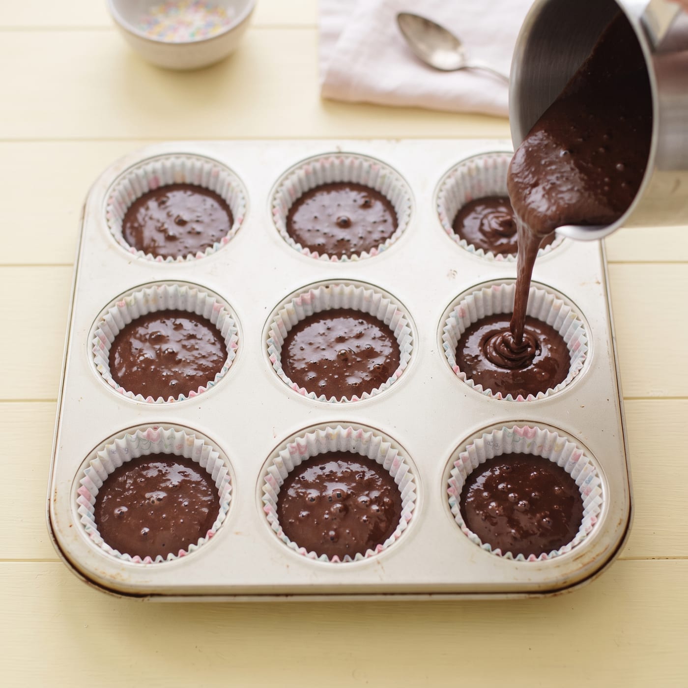 Chocolate cupcake batter being poured into paper liners in a muffin pan