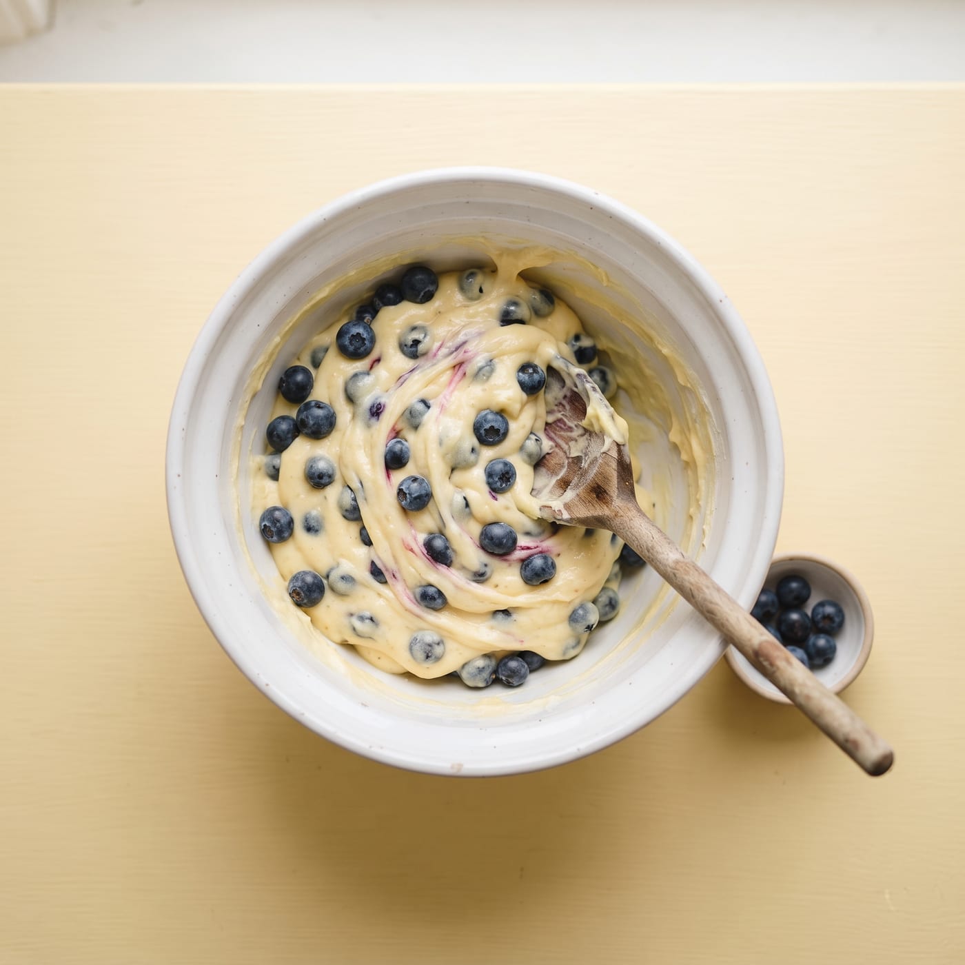 Fresh blueberries being folded into lemon cupcake batter in a mixing bowl