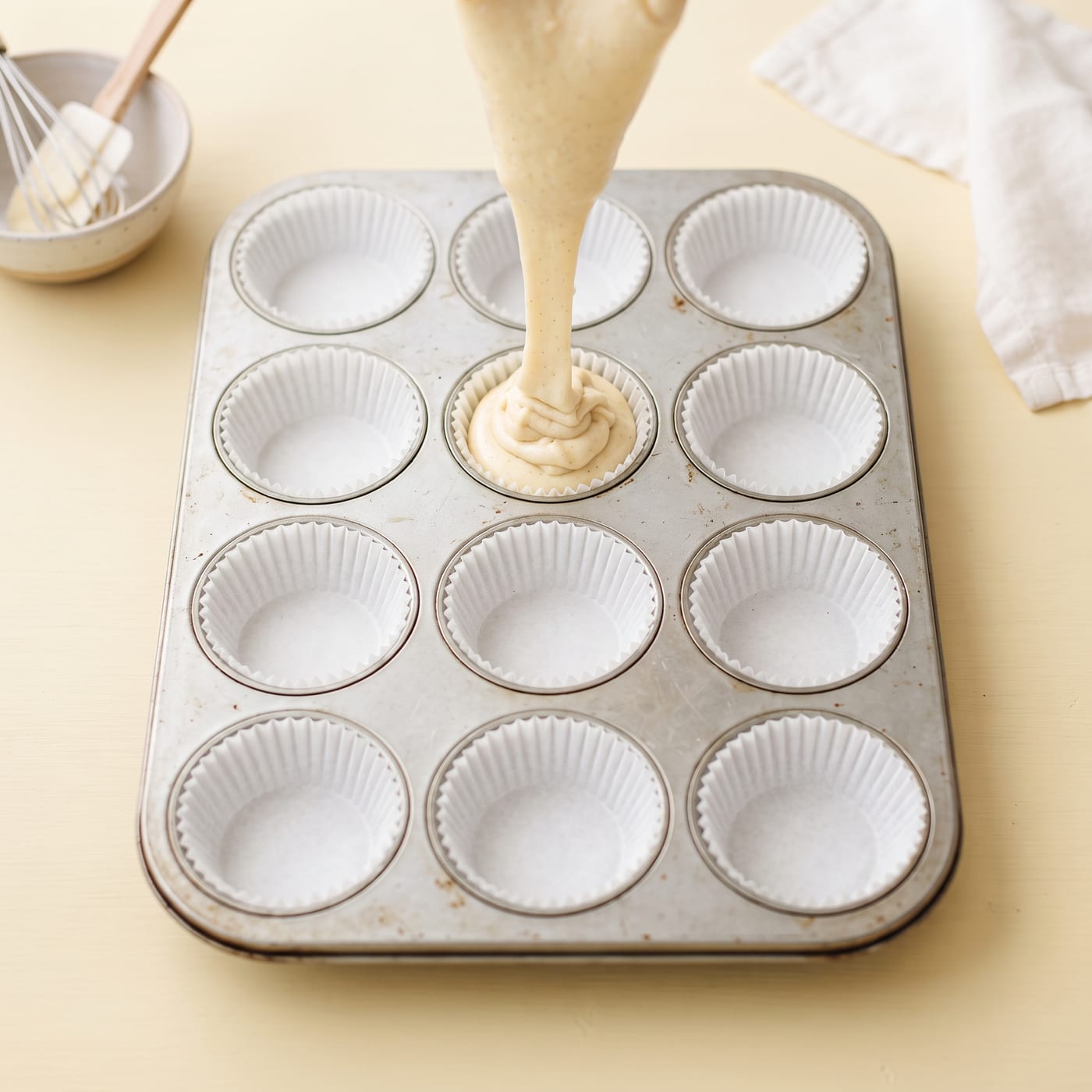 Vanilla cupcake batter being piped into paper liners in a muffin pan
