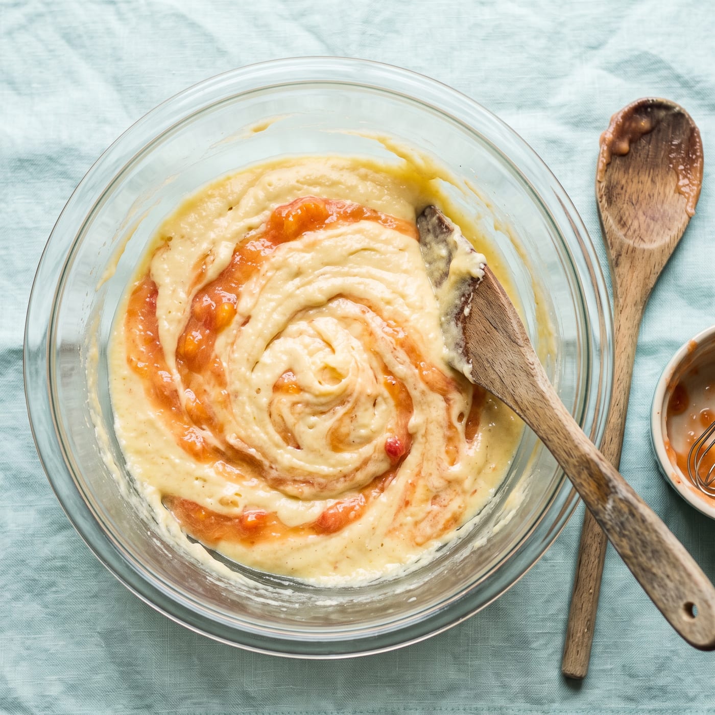 Fresh peach puree being folded into pale yellow cupcake batter in a glass mixing bowl
