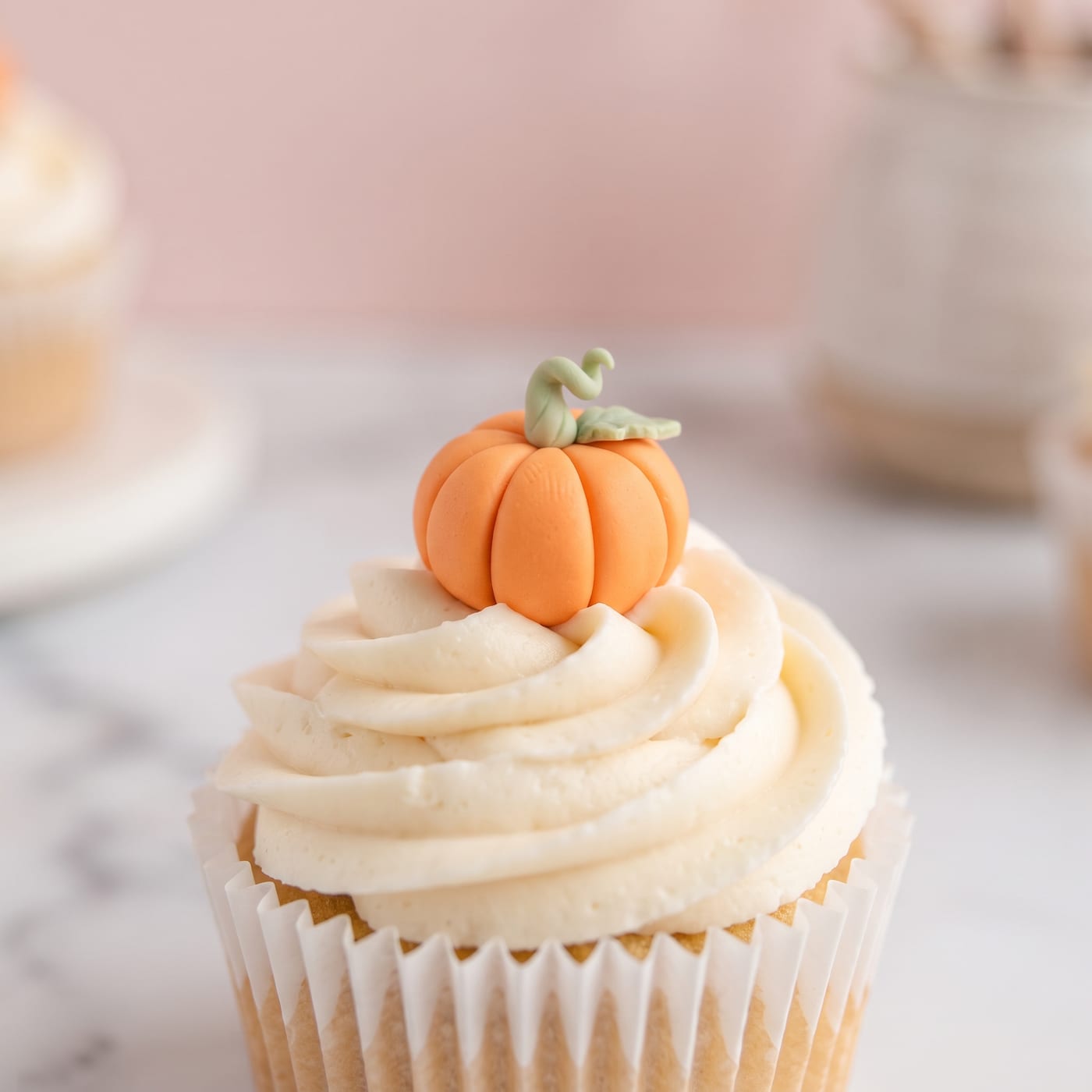 Close up of a tiny fondant pumpkin with green stem on top of cream cheese frosting