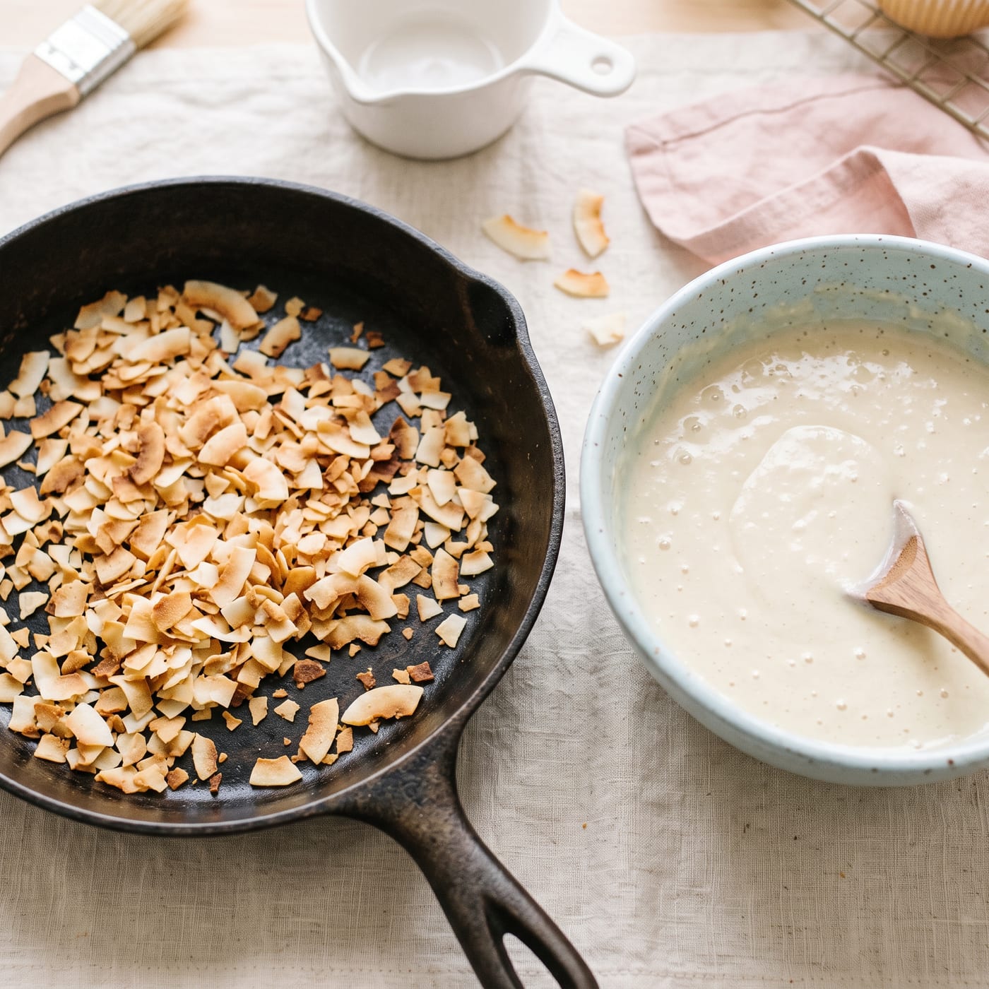 Toasted coconut flakes cooling in a skillet next to a bowl of coconut cupcake batter