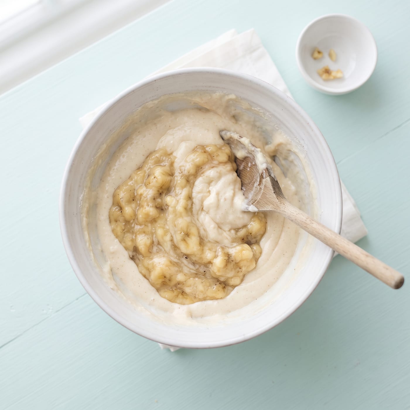 Mashed ripe bananas being folded into cupcake batter in a mixing bowl