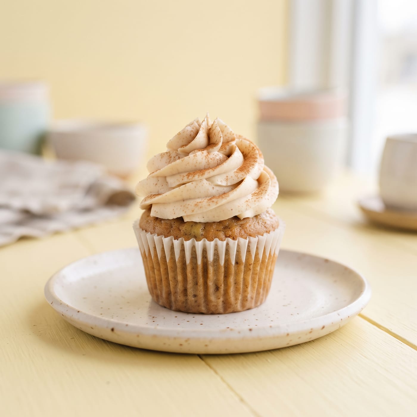 Vegan banana bread cupcake with tall swirled cinnamon cream frosting on a pastel background