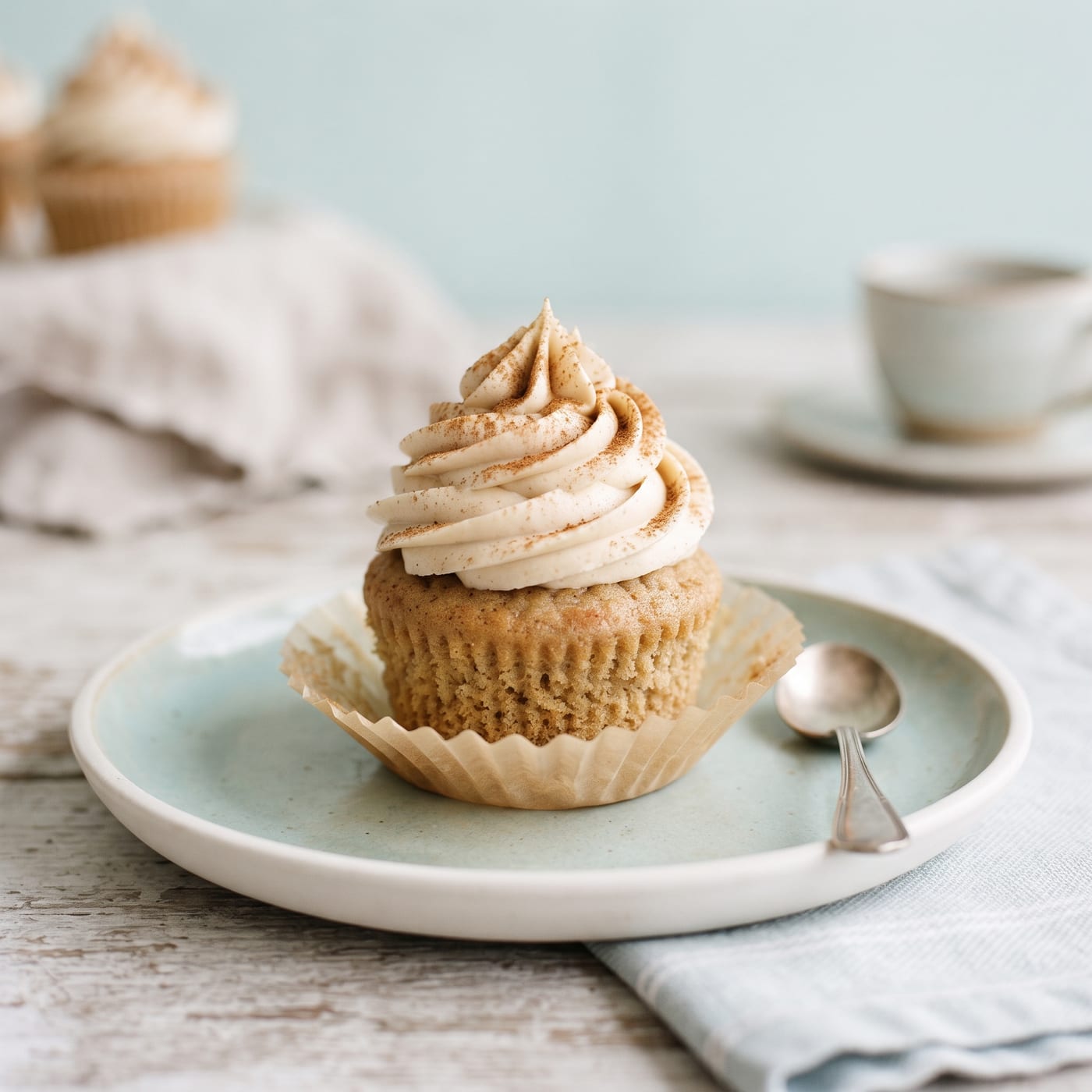 Vegan chai latte cupcake with tall swirled vanilla chai frosting and a cinnamon dusting on a pastel background