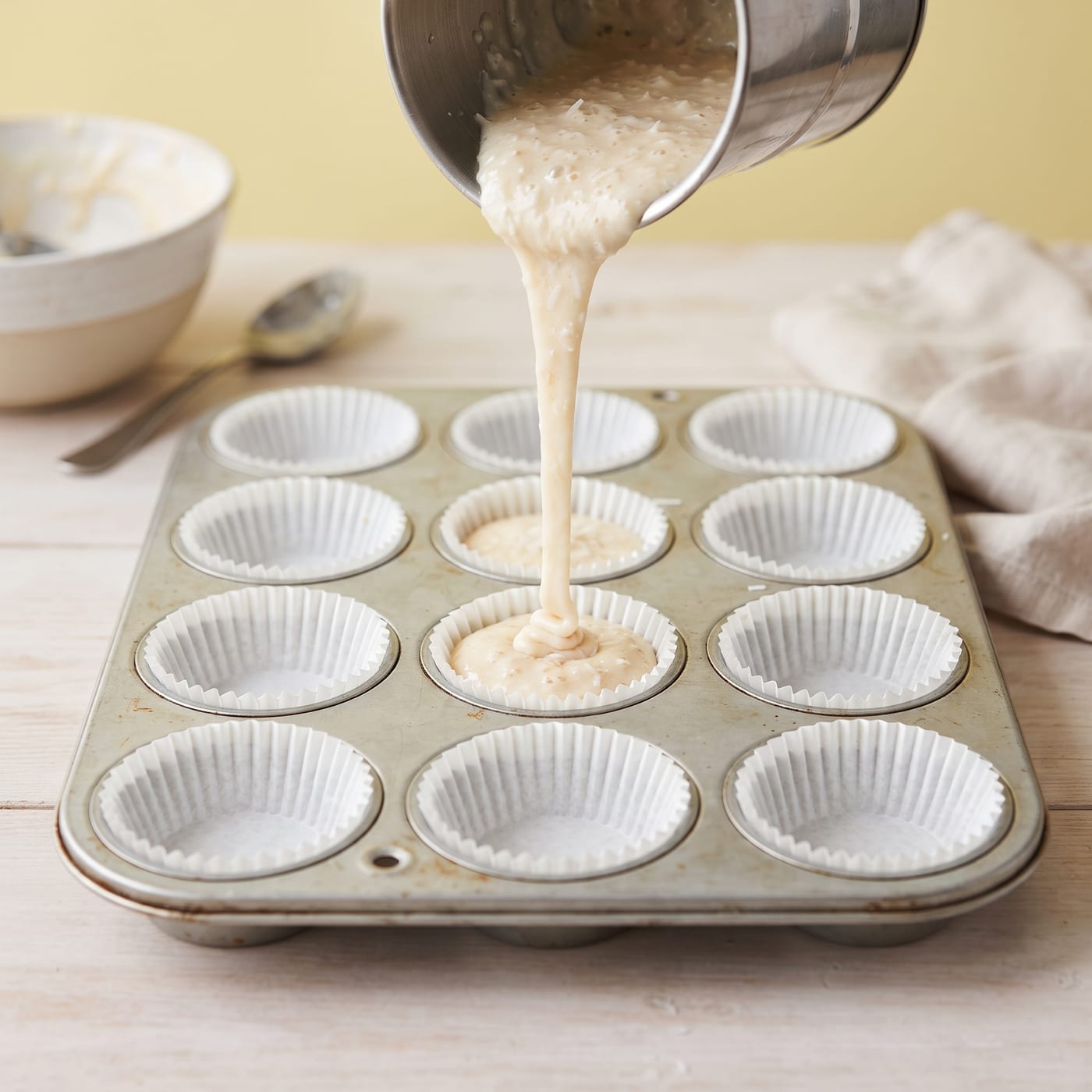 Coconut cupcake batter being poured into paper liners in a muffin pan