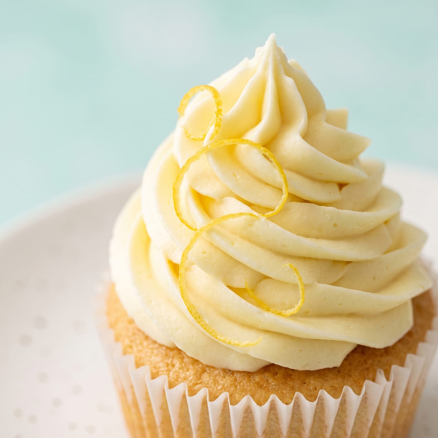 Close-up of lemon cream cheese frosting swirl with lemon zest garnish on a cupcake
