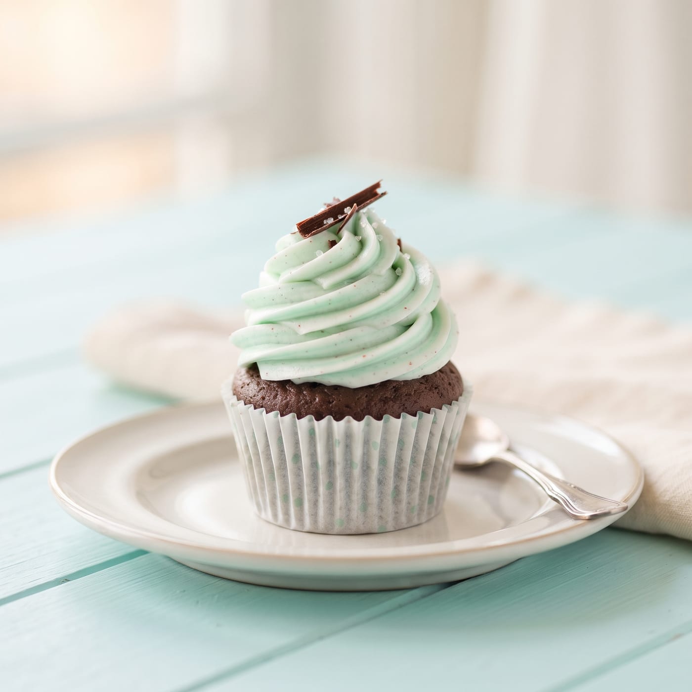 Vegan mint chocolate cupcake with tall swirled peppermint frosting on a pastel aqua background