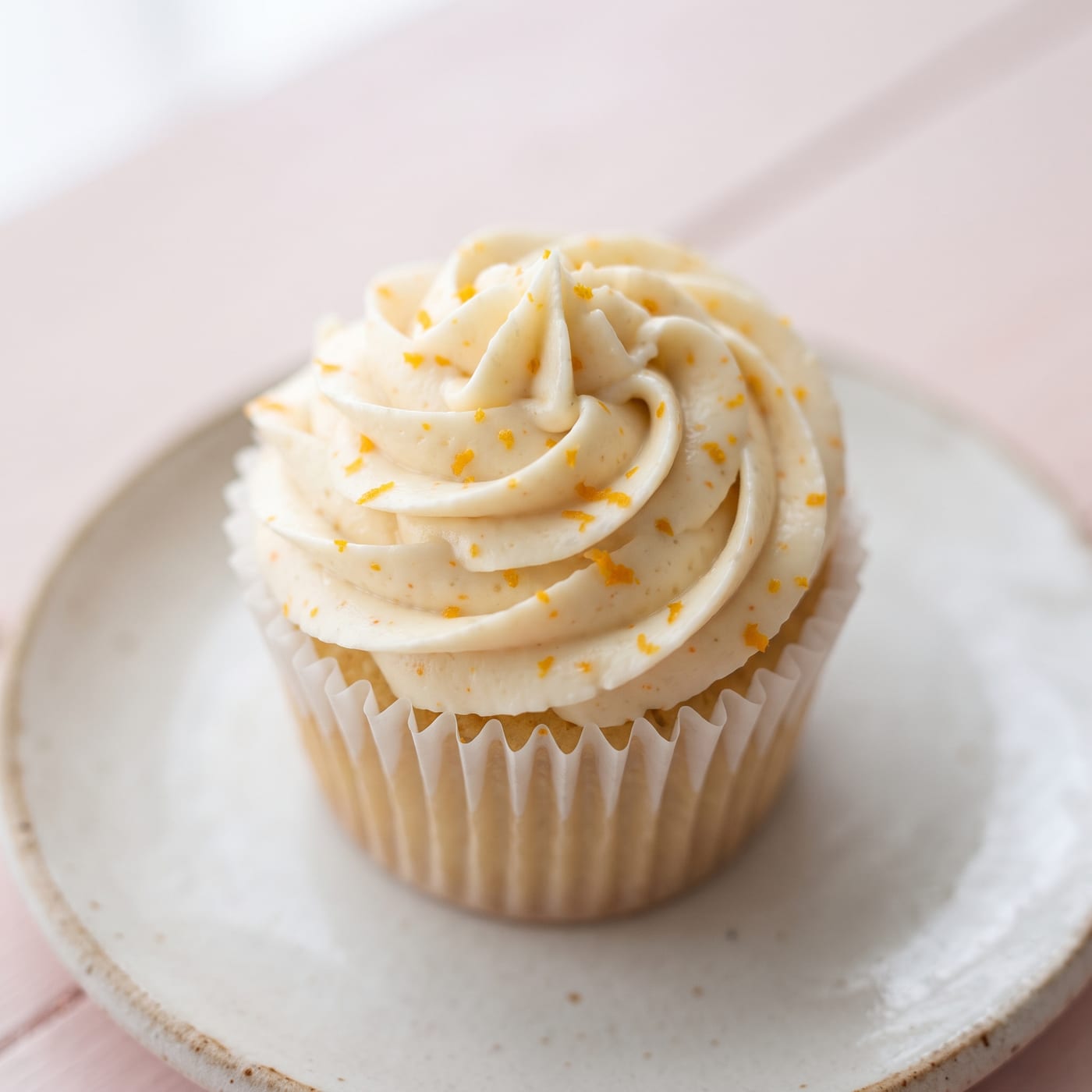 Close up of vanilla swirl frosting texture with orange zest flecks on a cupcake