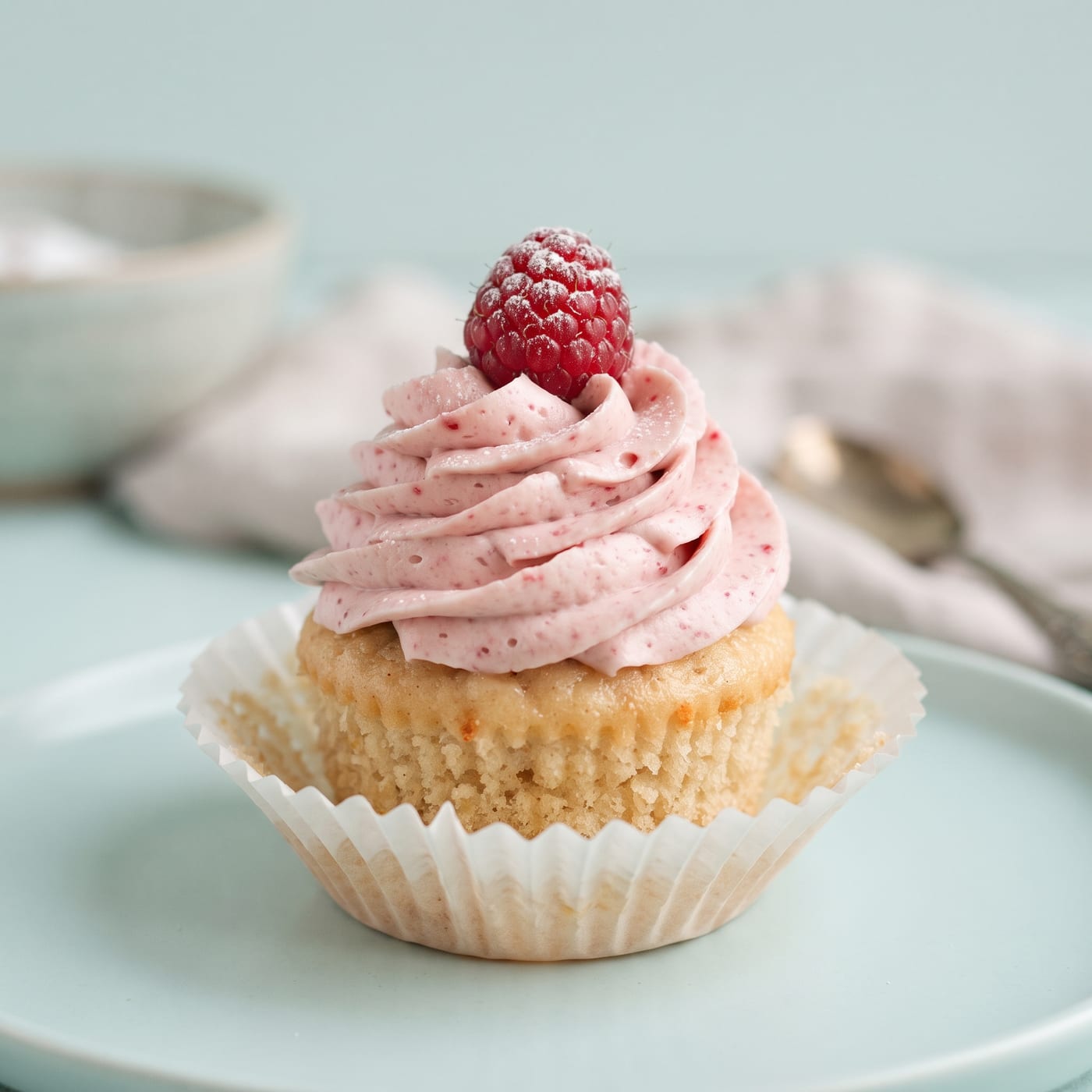 Close up of raspberry almond cupcake frosting swirl with a fresh raspberry garnish